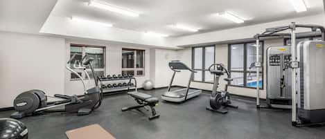A gym with treadmills, elliptical machines, free weights, and a yoga mat.