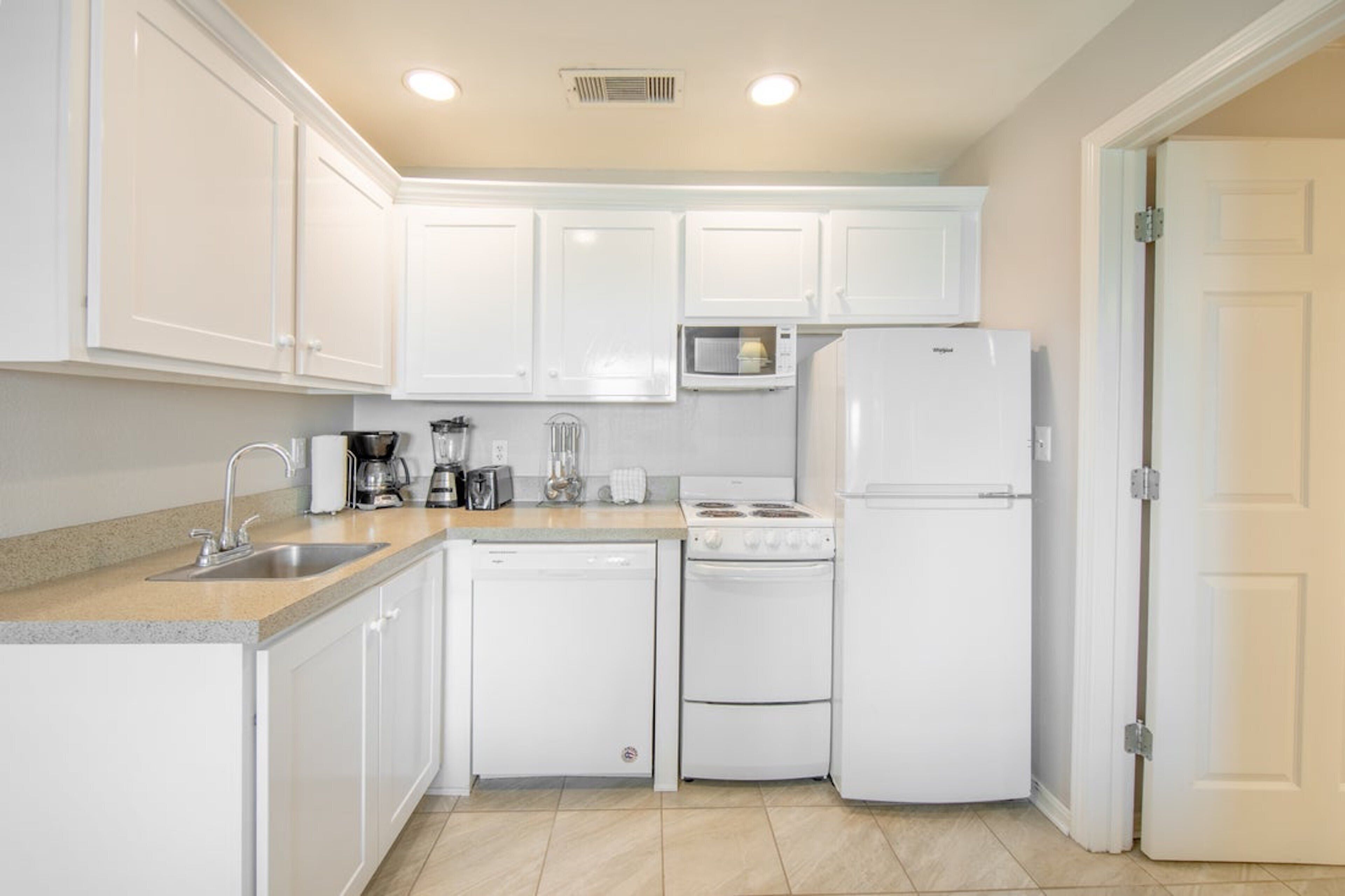 A compact kitchen with white cabinets, a microwave, a stove, a dishwasher, and a refrigerator.