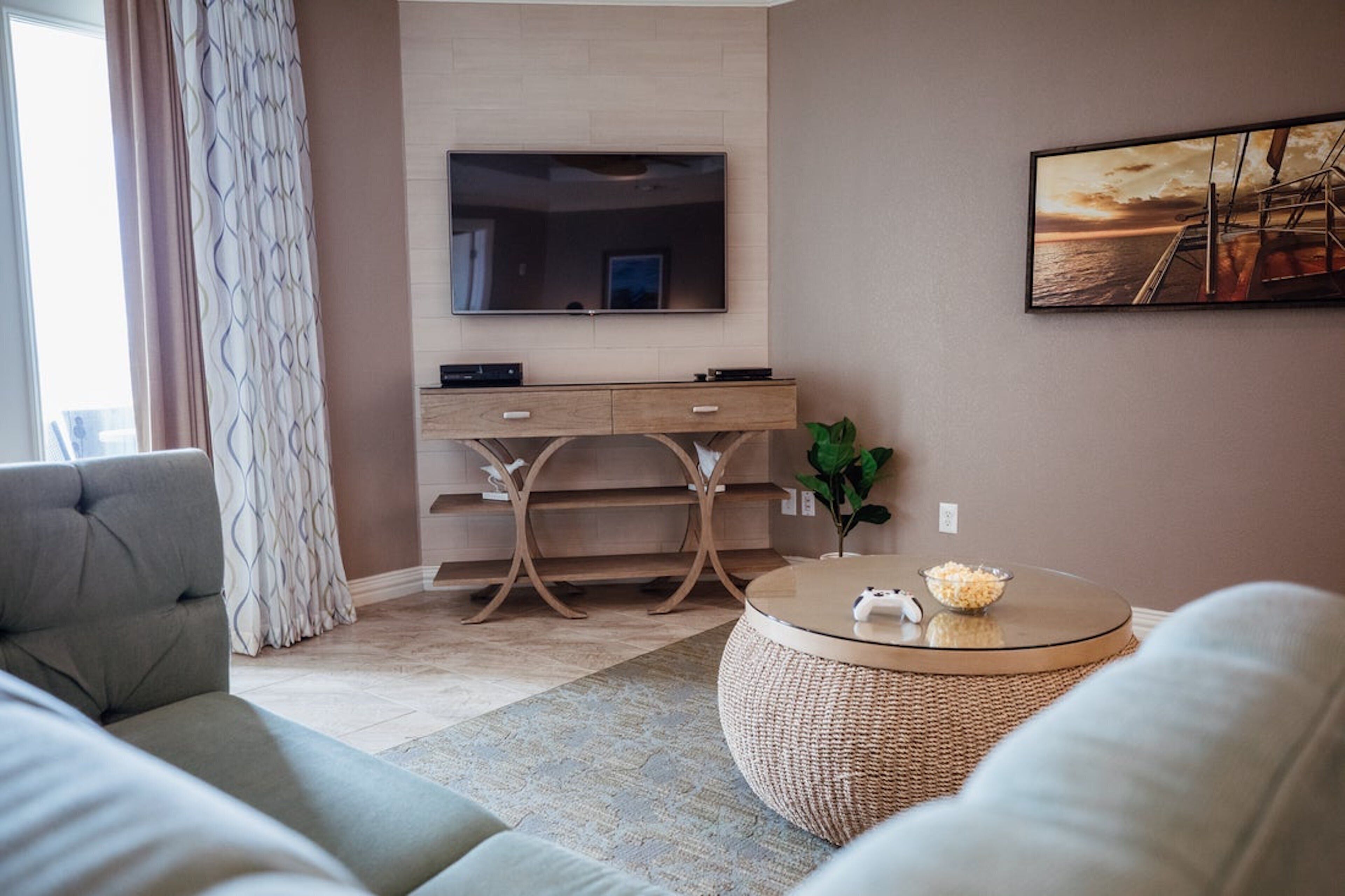 A modern living room with a flat-screen TV mounted on the wall, a comfortable sofa, a coffee table, and a decorative plant.