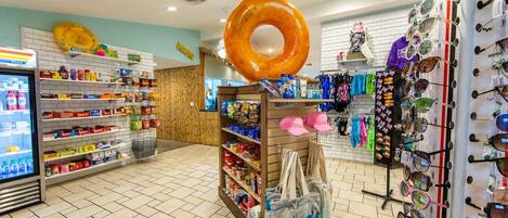 A store interior with shelves stocked with snacks, a refrigerated section, and a display of sunglasses and hats.