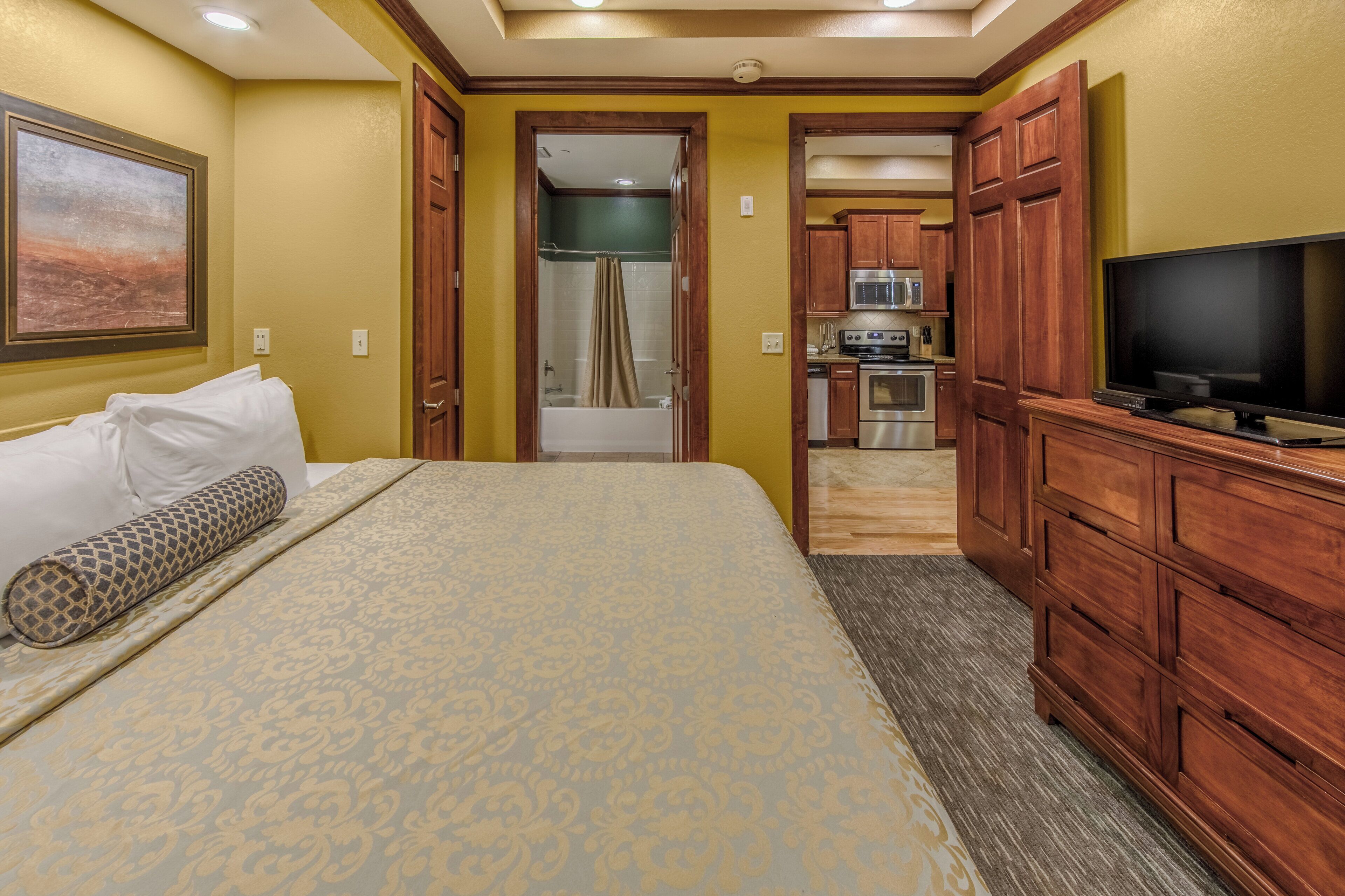 Une chambre d’hôtel équipée d’un lit, d’une télévision, d’armoires en bois et d’une kitchenette.