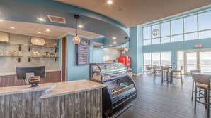 Un café moderne avec un comptoir en bois, une vitrine remplie de pâtisseries et un tableau affichant le menu.
