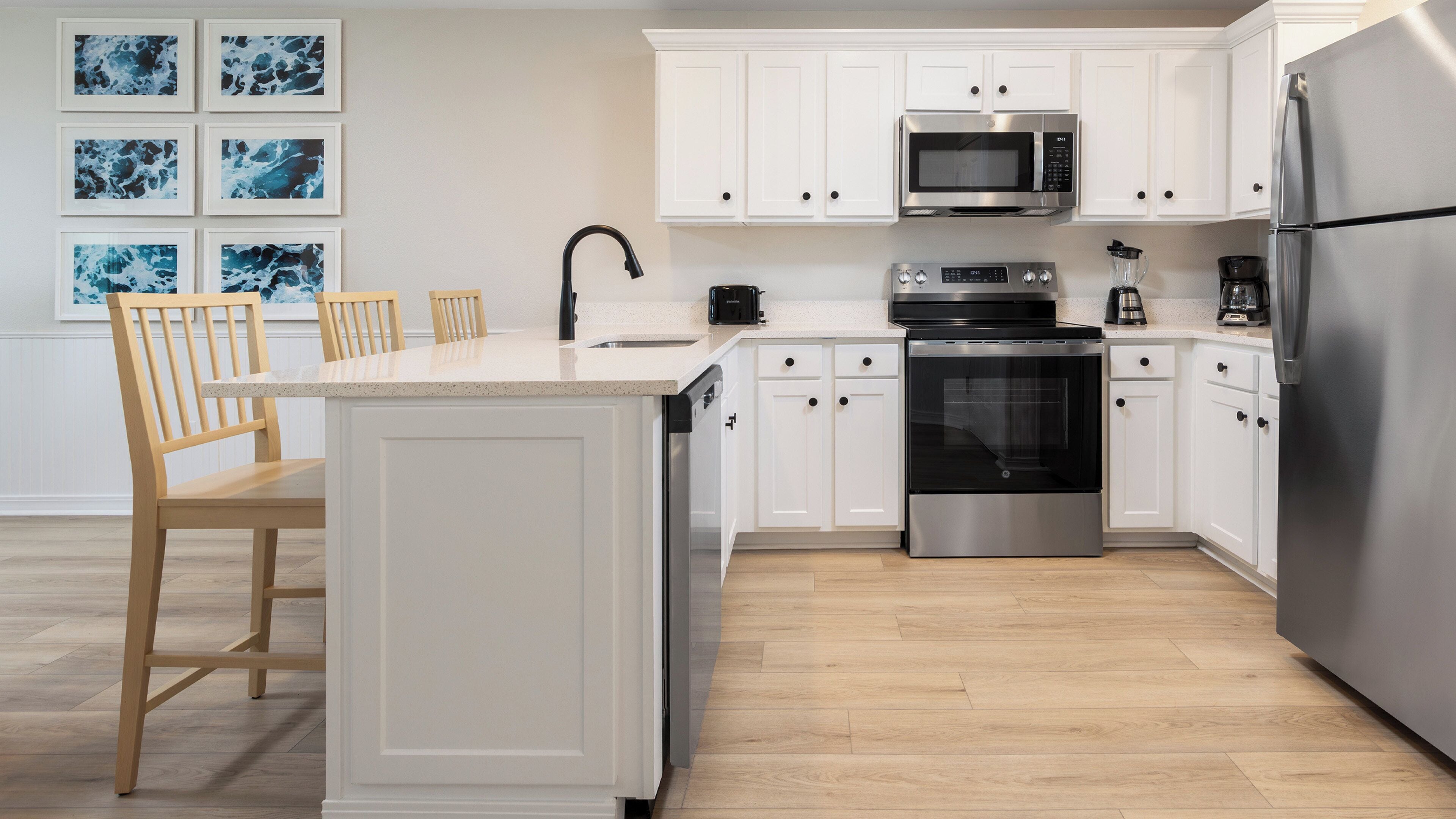 A modern kitchen with white cabinetry, stainless steel appliances, and a wooden dining area.