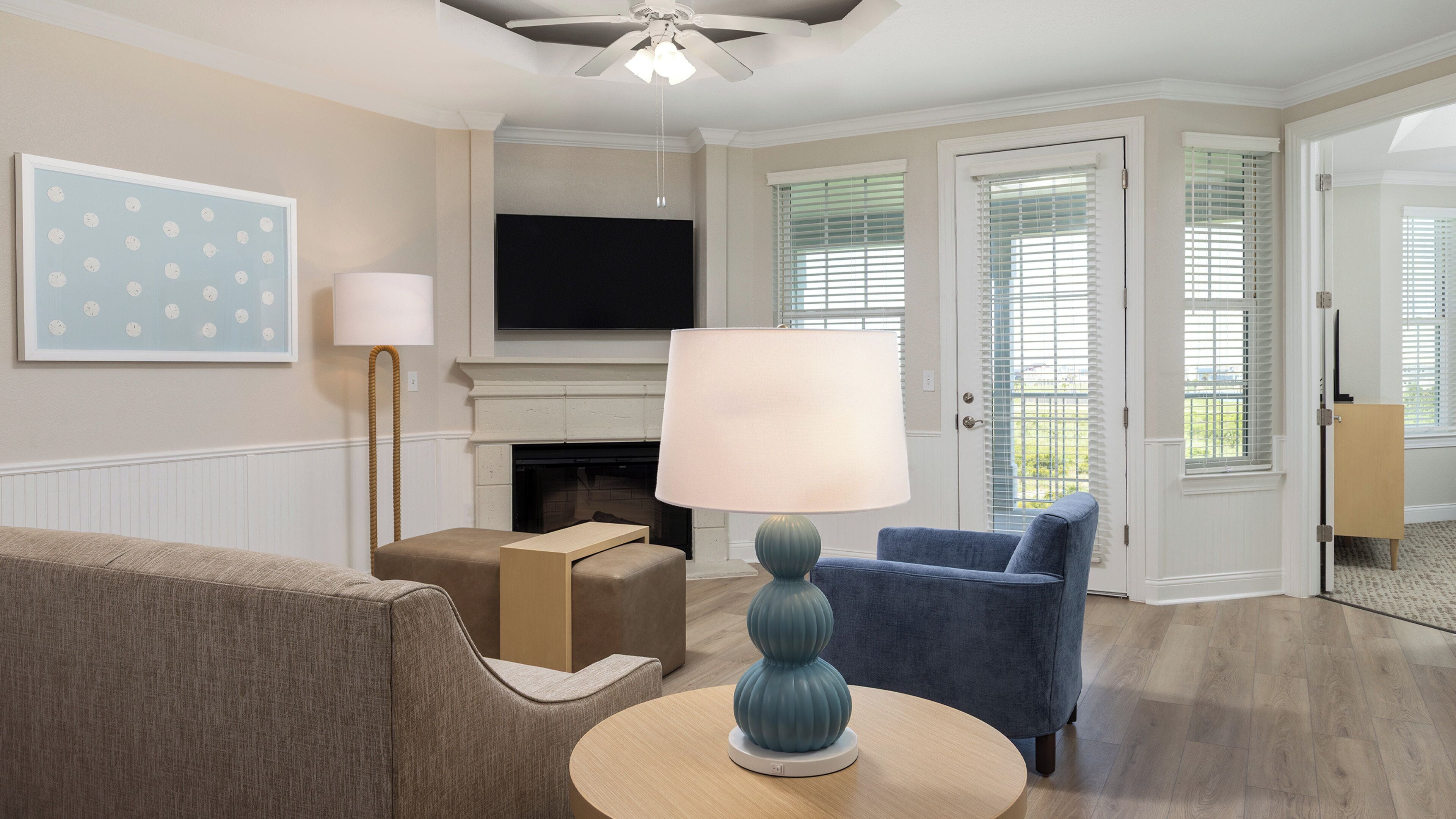 Una sala de estar con chimenea, televisor, un sillón azul, una lámpara y un sofá.