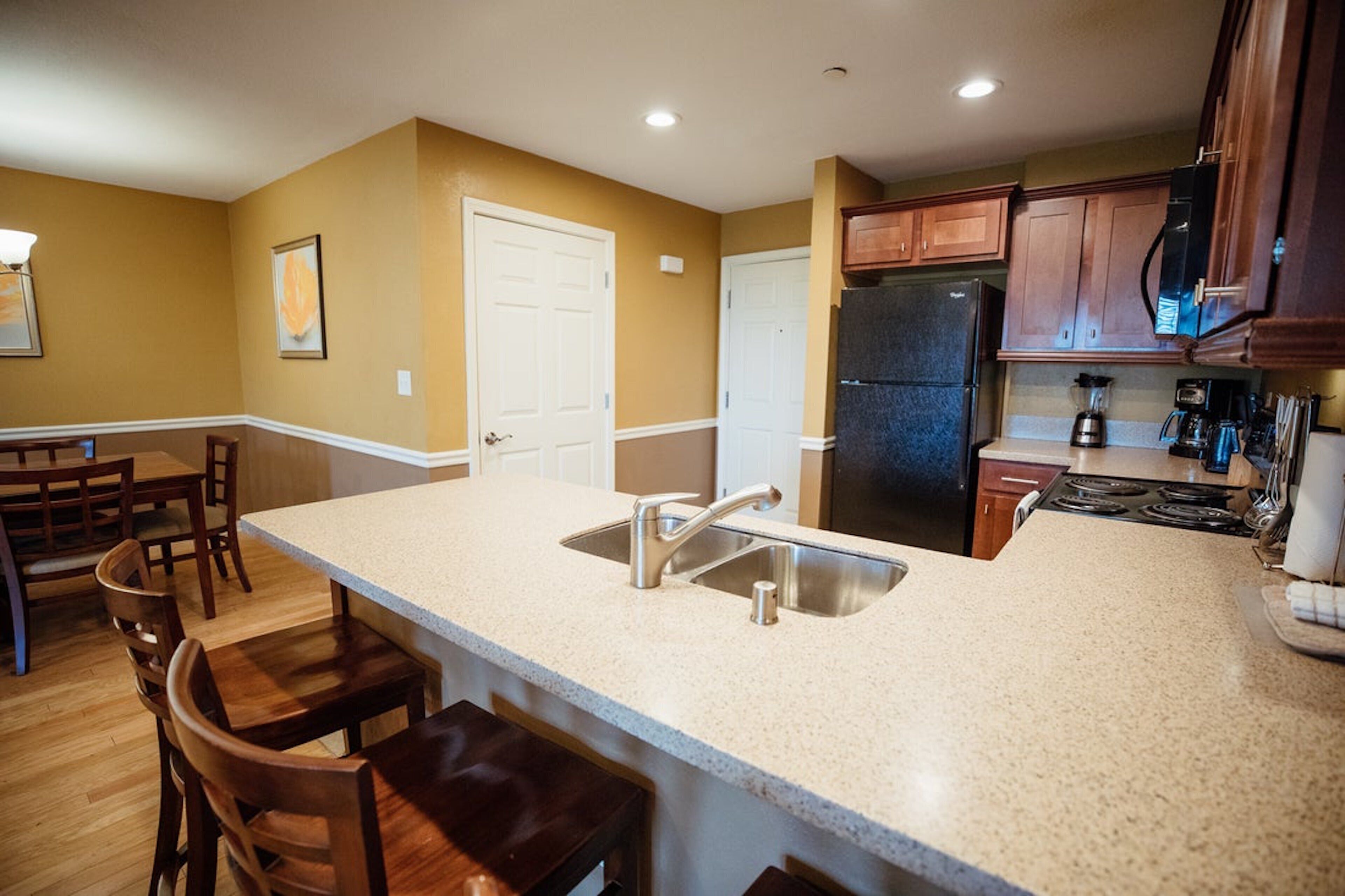 Una cocina con una isla grande, electrodomésticos de acero inoxidable, armarios de madera y una zona de comedor con sillas.