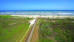 Een kustlandschap met een zandstrand, een houten vogel kijken en een heldere blauwe lucht.