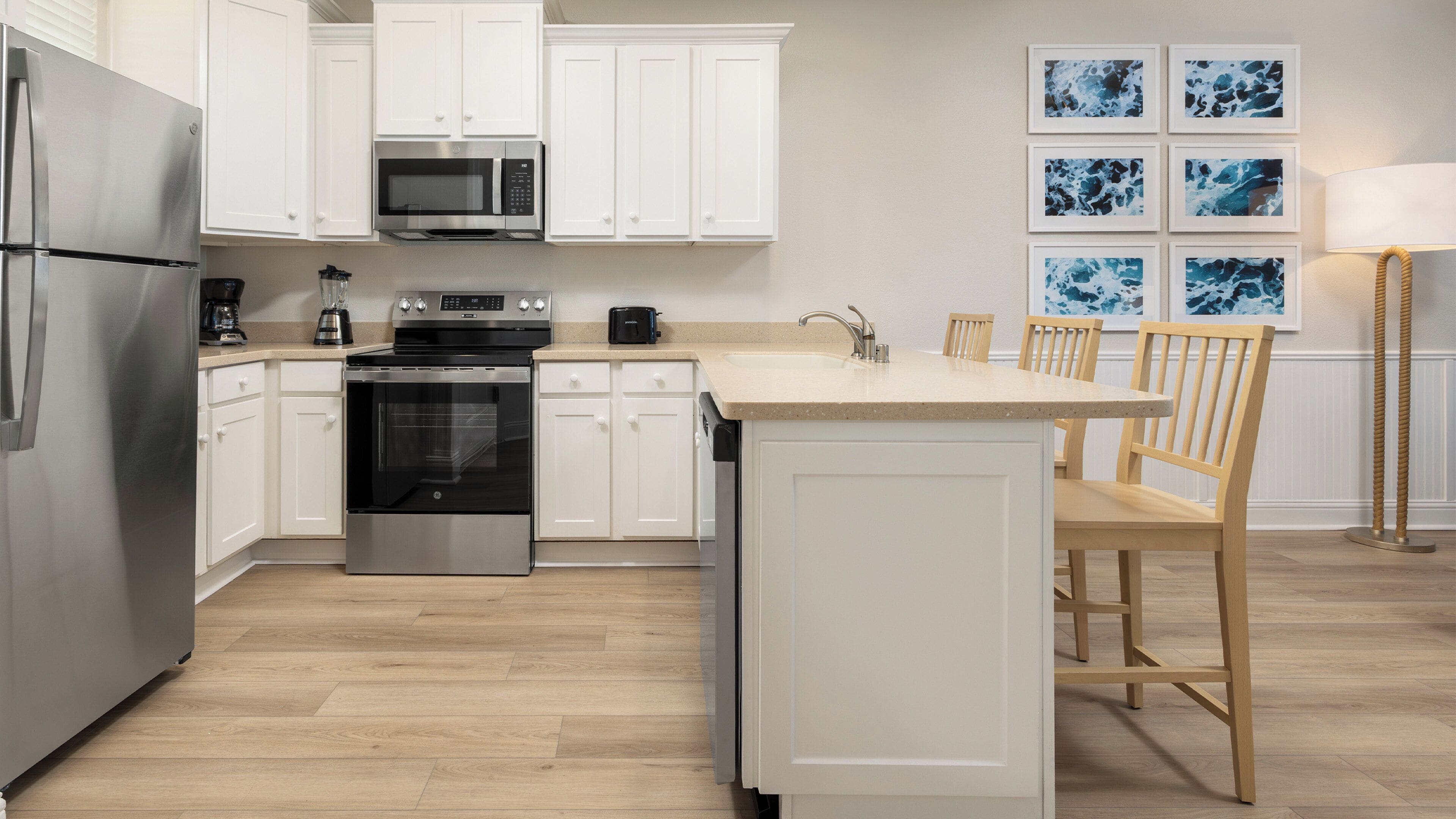A modern kitchen with white cabinetry, stainless steel appliances, a central island, and wooden chairs.