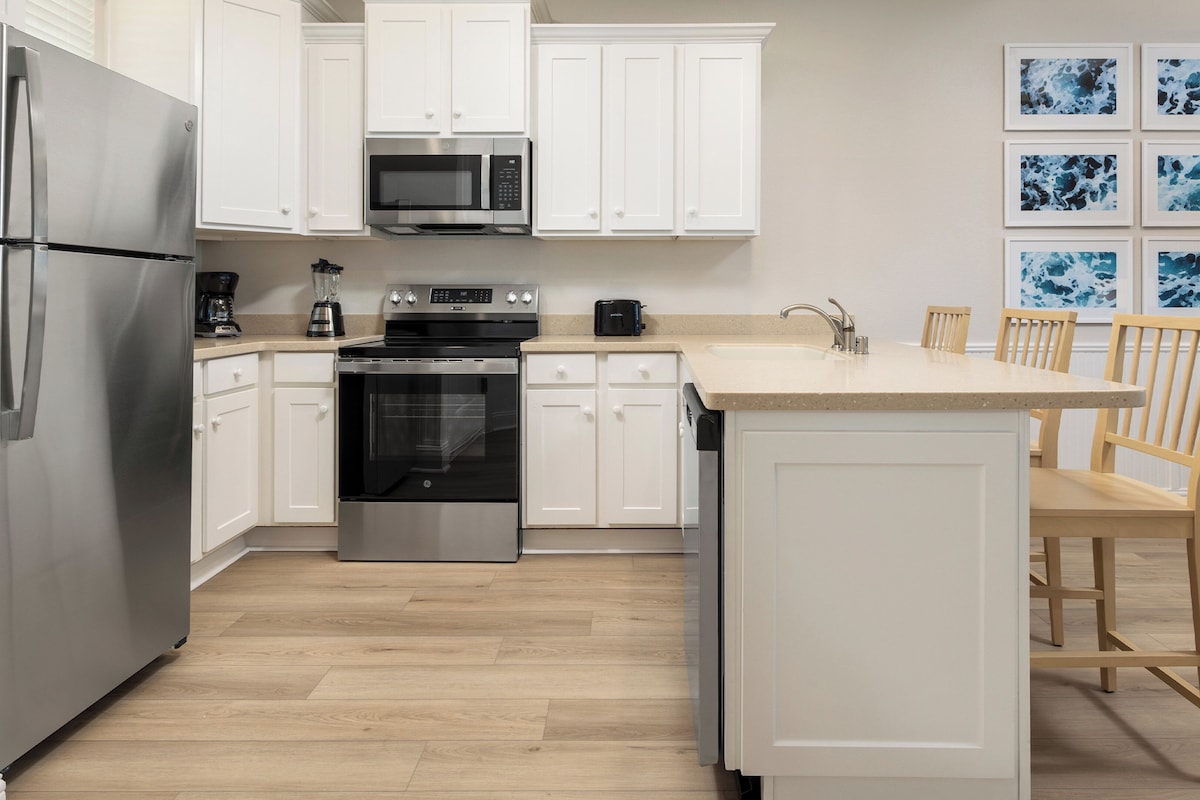 Une cuisine moderne avec des meubles blancs, des appareils en acier inoxydable, un îlot central et des chaises en bois.