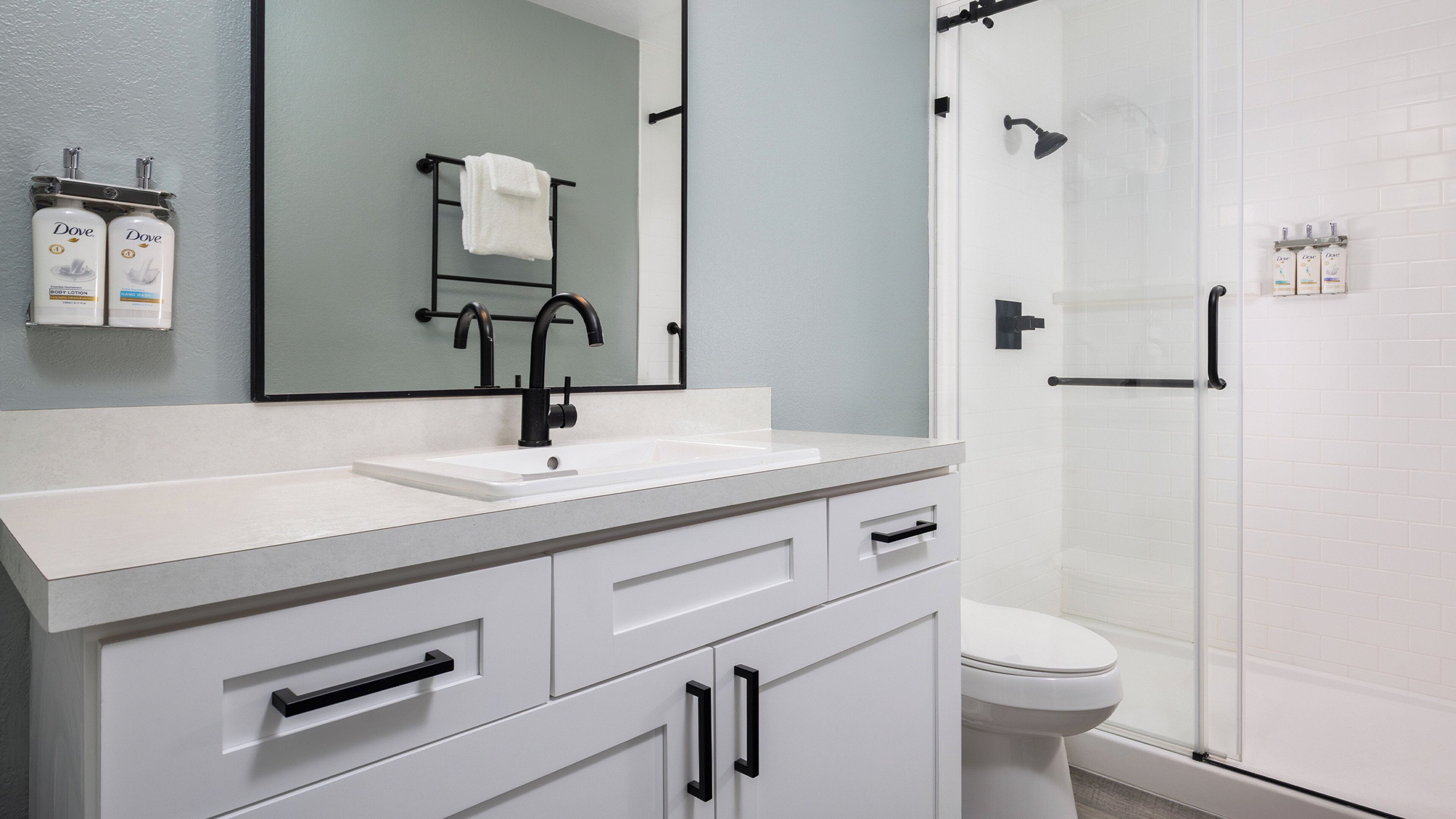 Un baño moderno con lavamanos blanco, grifo negro y cabina de ducha de vidrio.