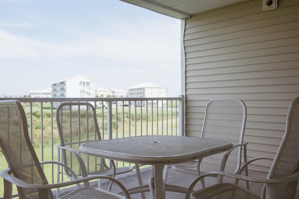 Un balcon avec une table ronde et quatre chaises, donnant sur un espace verdoyant avec des bâtiments en arrière-plan.