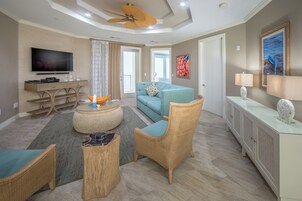 Un salon moderne comprenant un téléviseur, un canapé, des fauteuils en osier et une table basse en verre.