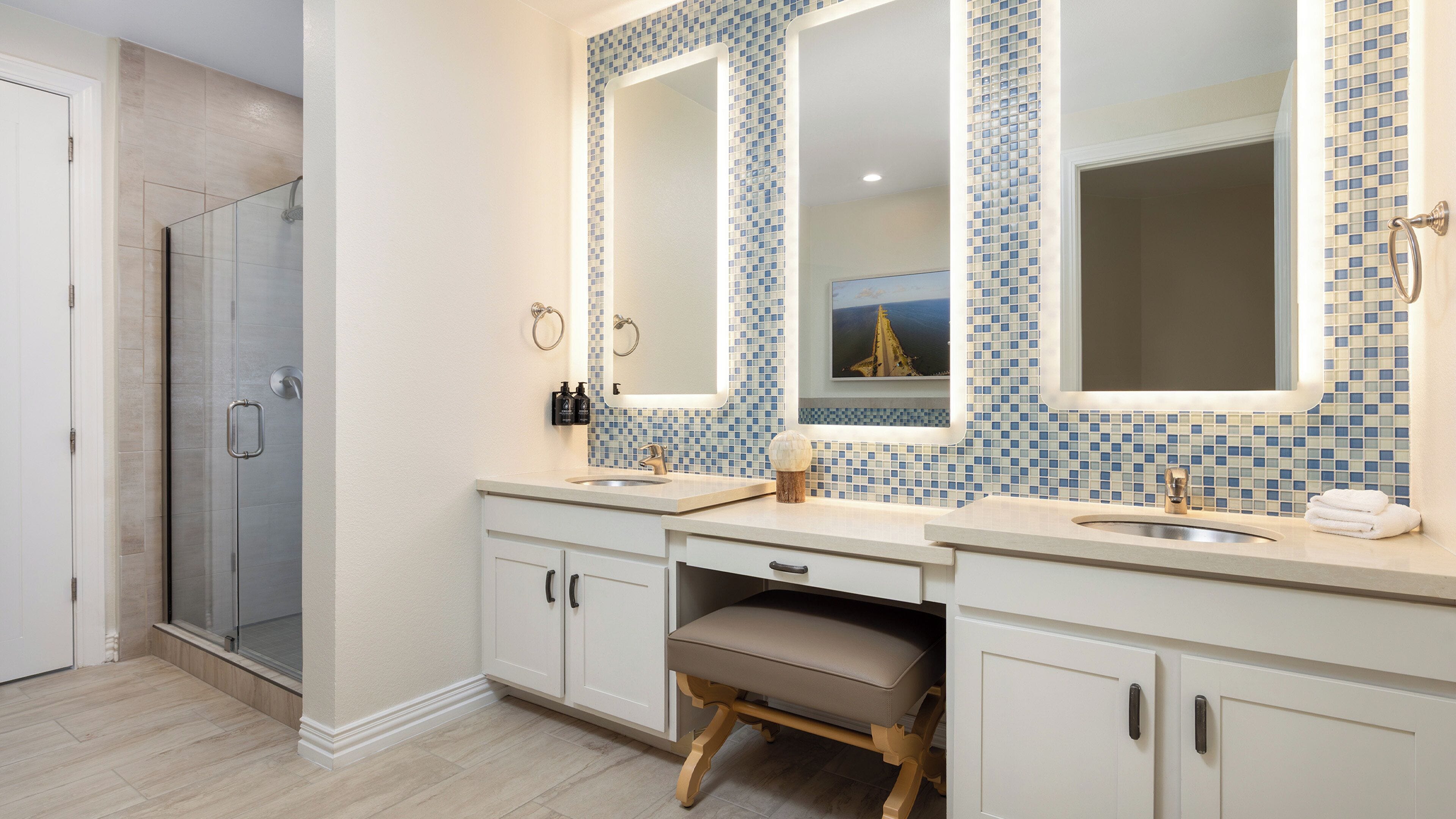 A bathroom with two sinks, a shower, and a vanity with a stool.