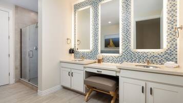 A bathroom with two sinks, a shower, and a vanity with a stool.