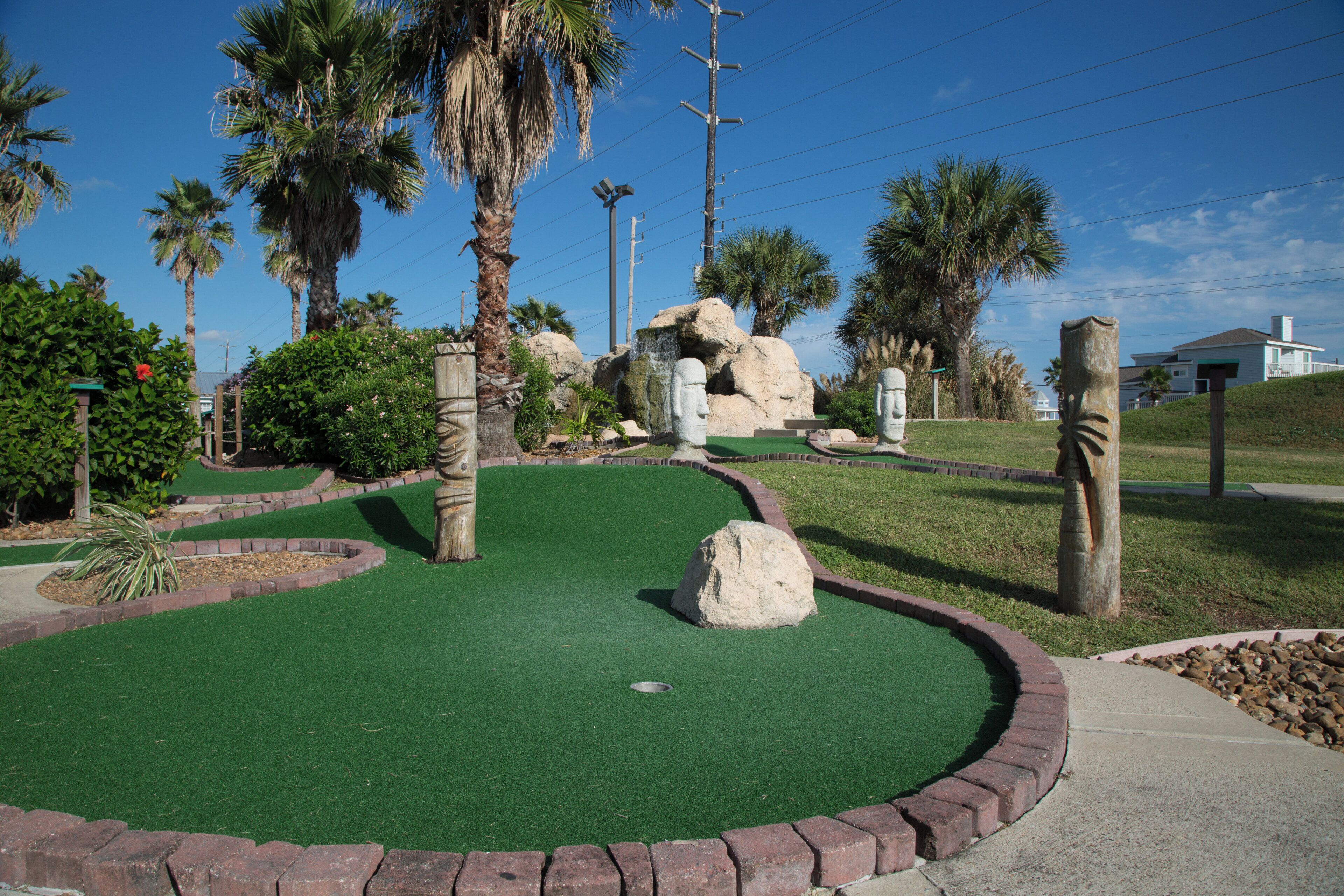 Un parcours de minigolf avec un gazon synthétique vert, des palmiers et une formation rocheuse.