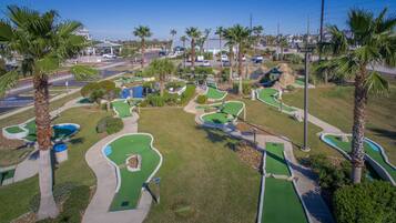 Campo de golf con varios hoyos, palmeras y un aparcamiento.