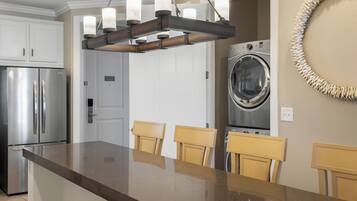 A kitchen with a stainless steel refrigerator, a built-in oven, a wooden island with chairs, and a washing machine.