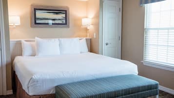 Habitación de hotel con una cama grande, un banco, dos lámparas de pared, una puerta y una ventana con persianas.
