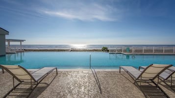 Una piscina con vista al océano, dos sillas de descanso y una cerca blanca.