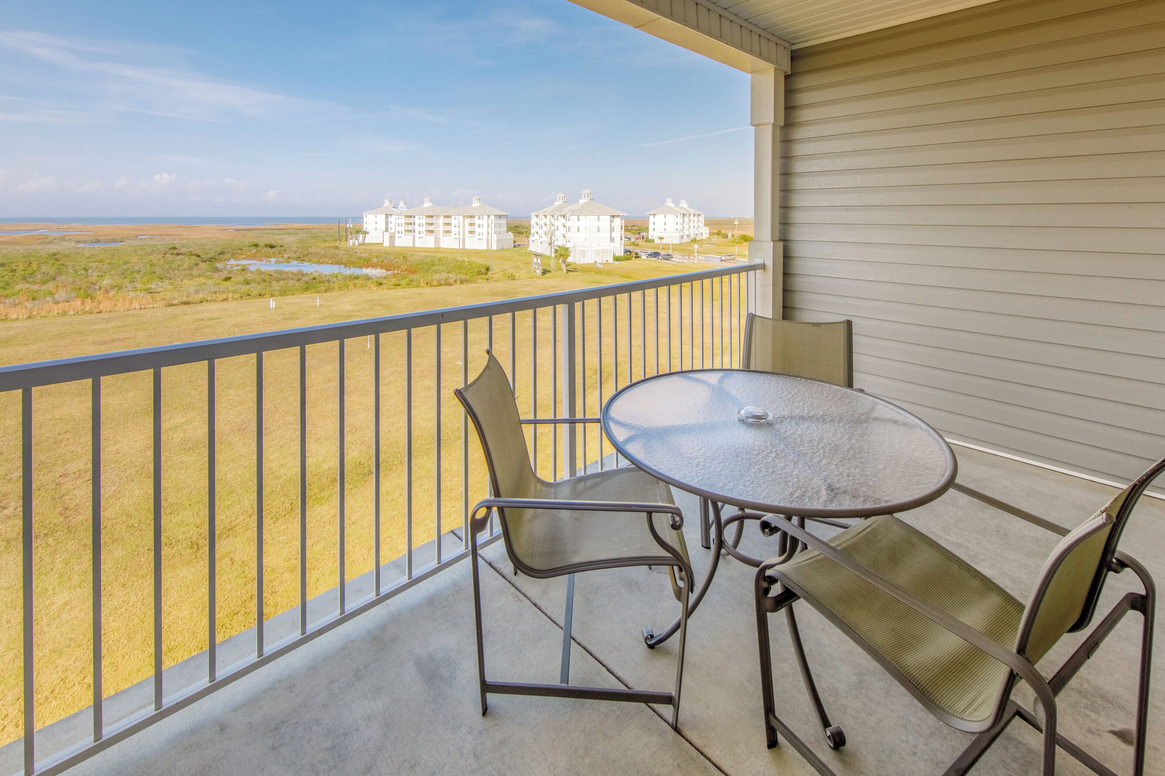A balcony with a table and chairs, overlooking a grassy area and buildings.
