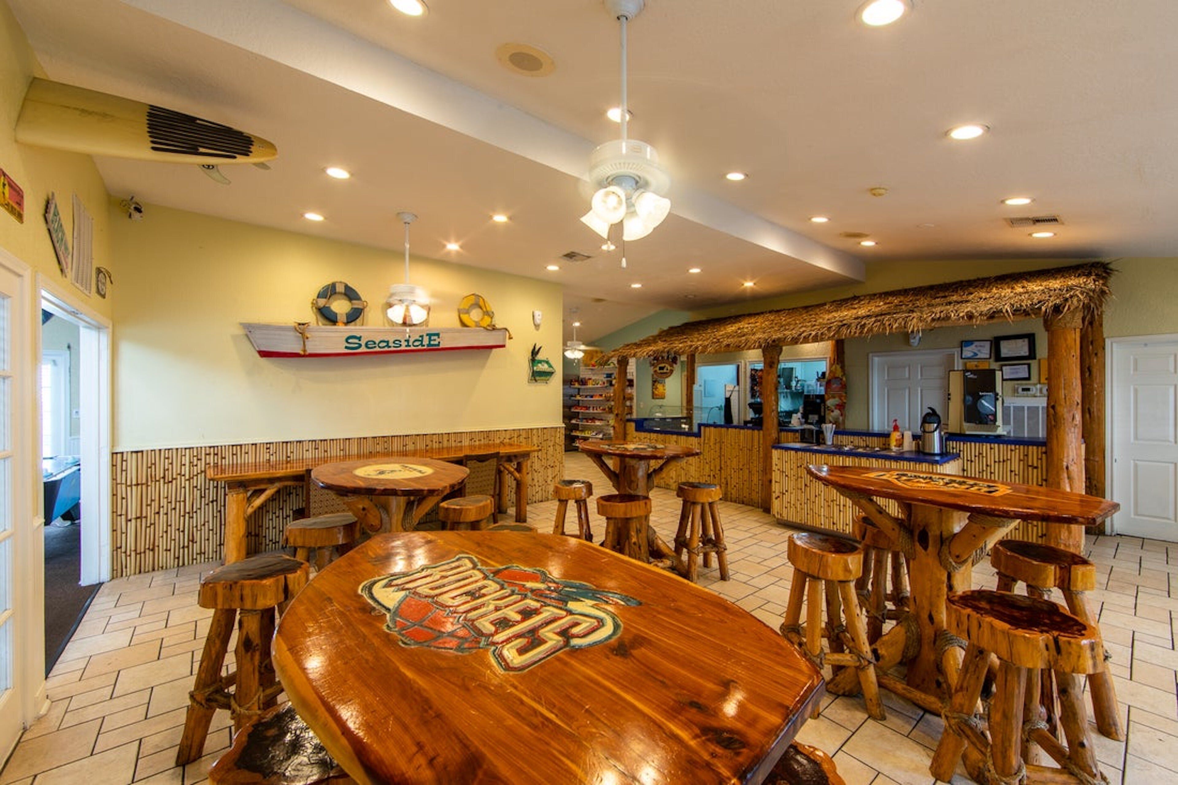 A restaurant interior with wooden tables and stools, a bar area, and a ceiling fan.