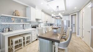 Une cuisine moderne avec des meubles blancs, un grand îlot central doté de tabourets et un pare-feu en carreaux.