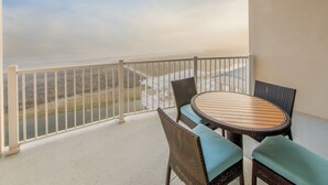 A balcony with a view of a body of water and a distant shoreline. There is a round table with two chairs and a small railing.