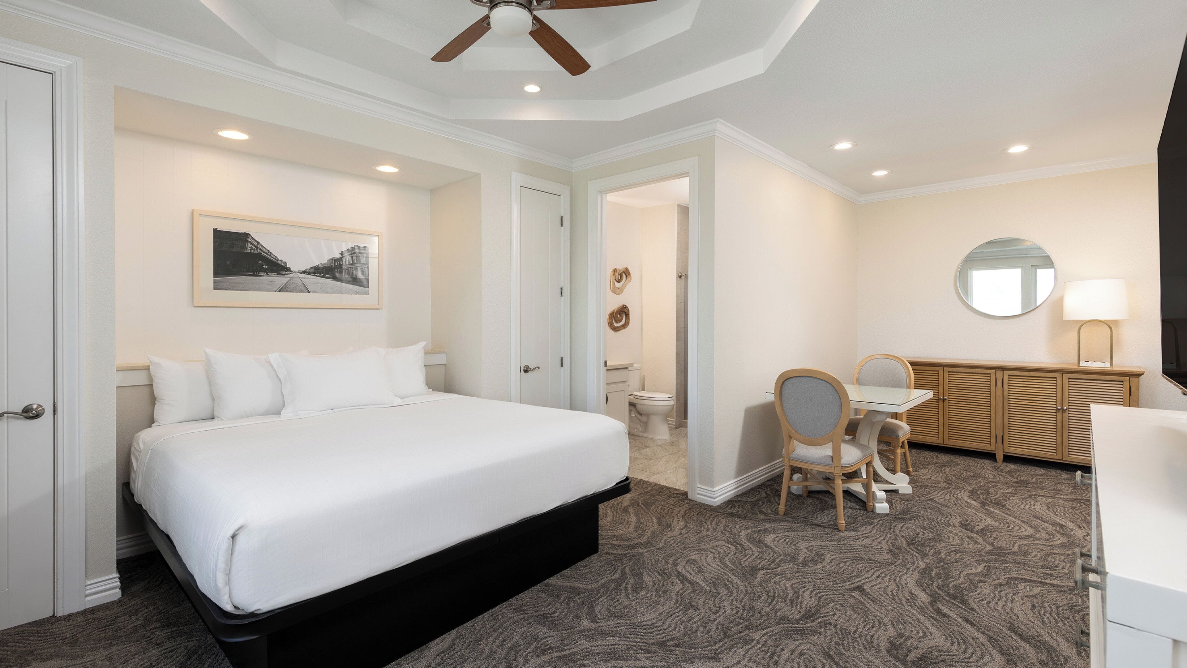 Una habitación de hotel con una cama grande, un escritorio con dos sillas, un baño y un ventilador de techo.