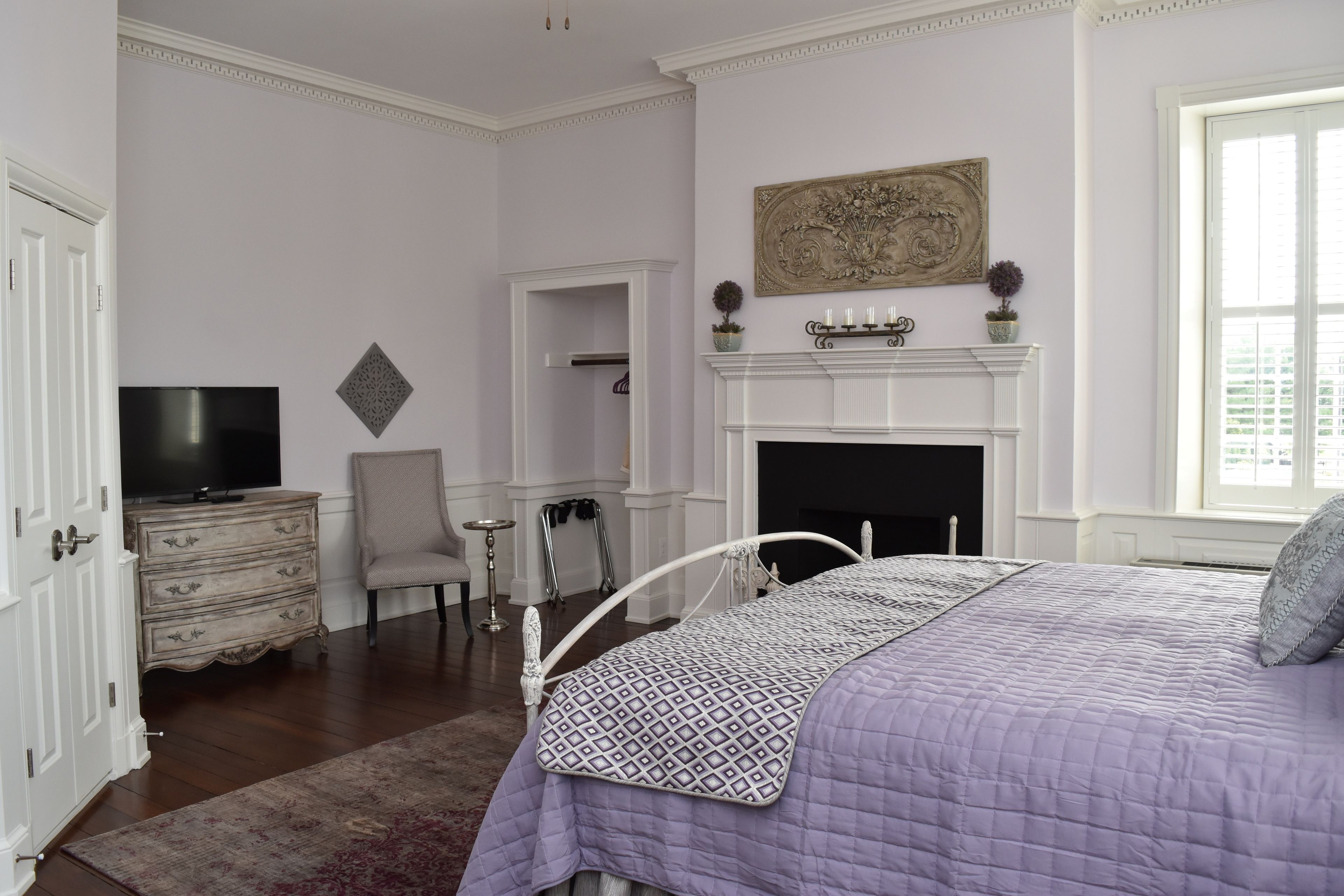 A bedroom with a bed, dresser, TV, fireplace, and a window.