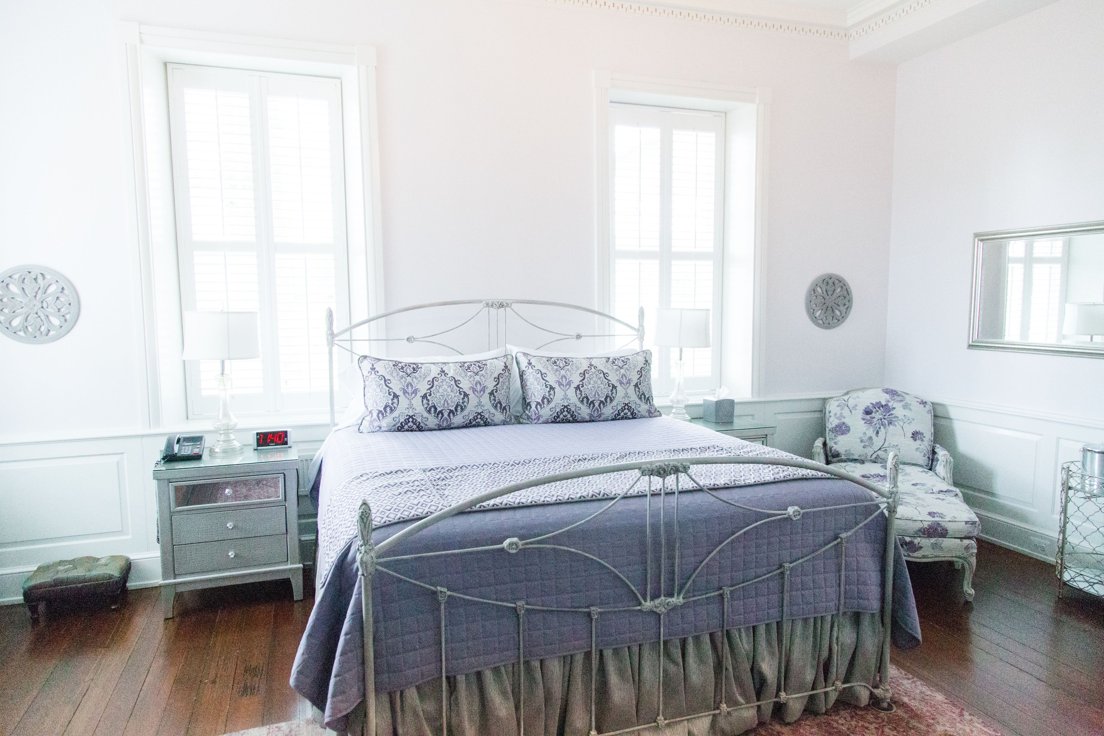 A neatly arranged bedroom with a metal bed frame, a bedside table with a lamp, and a chair.