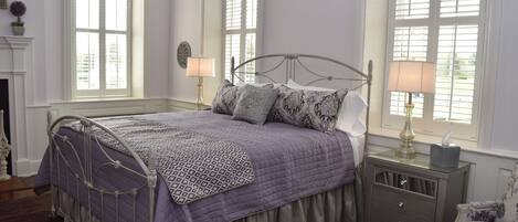 A bedroom with a bed, nightstands, a chair, and large windows.