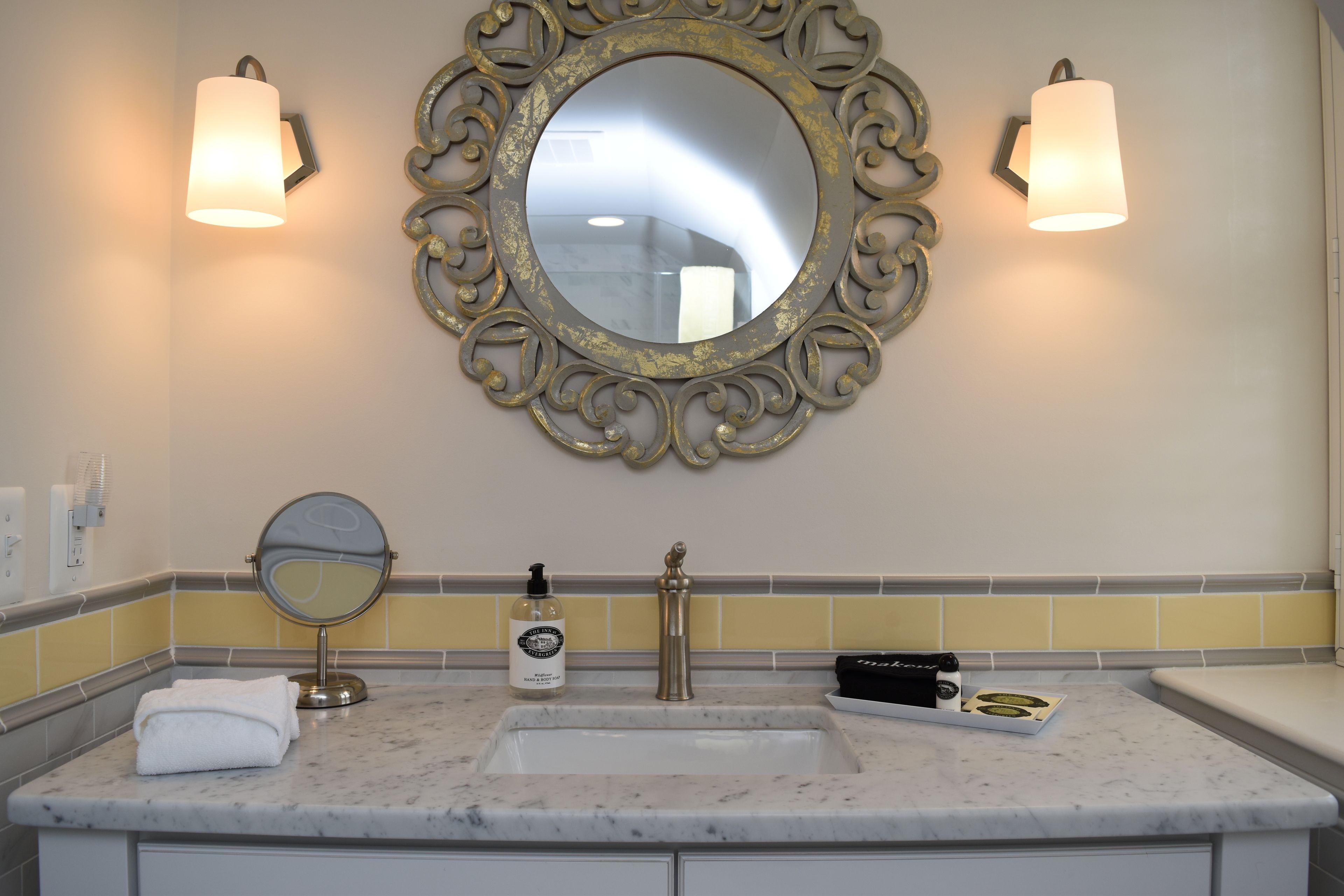 A bathroom with a marble sink, a gold-framed mirror, two wall-mounted lights, and a towel on the counter.