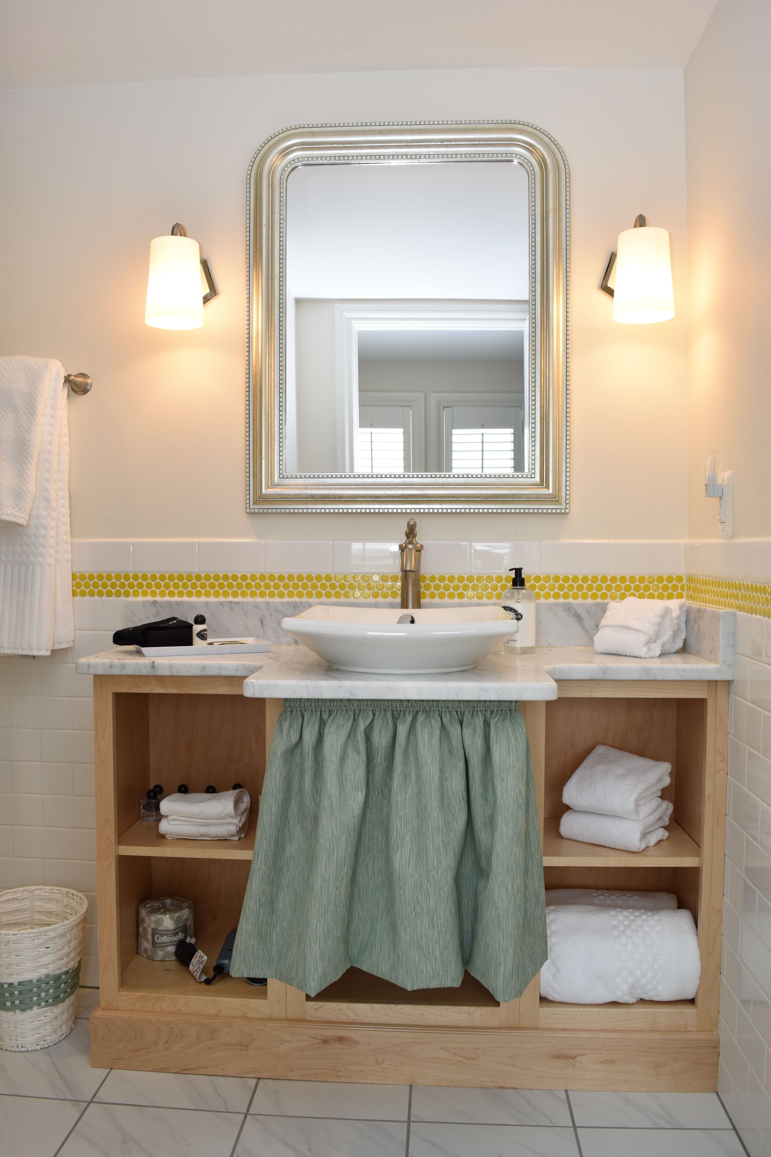 A bathroom with a white sink, a mirror with a gold frame, and a wooden vanity with shelves.