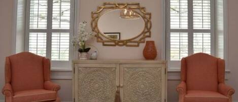 Une pièce comprenant deux fauteuils assortis, un meuble décoratif orné de sculptures complexes et un grand miroir placé au-dessus.