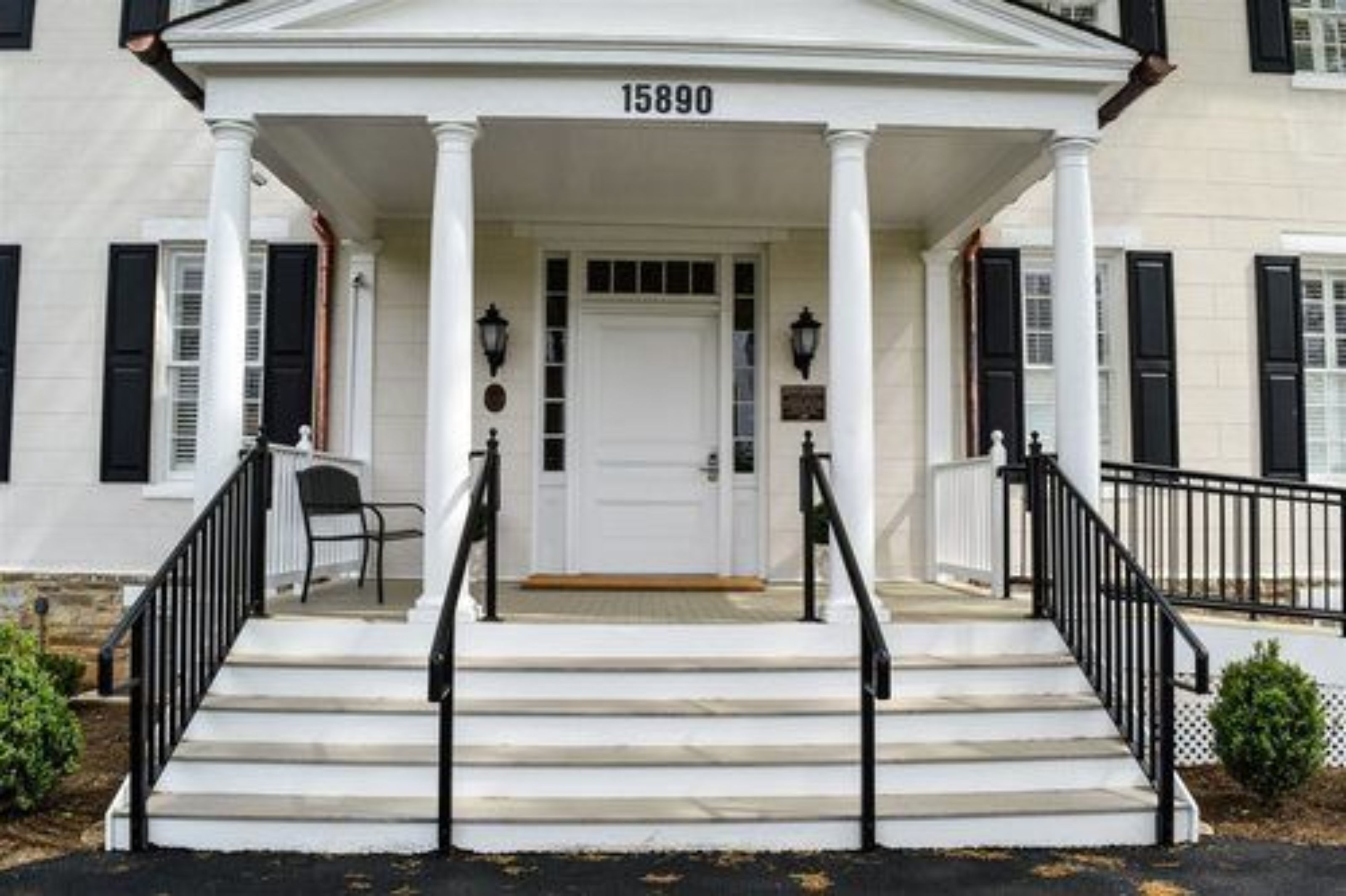 Un bâtiment blanc avec le numéro « 15890 » au-dessus de l’entrée, un porche avec des marches et une rambarde noire.