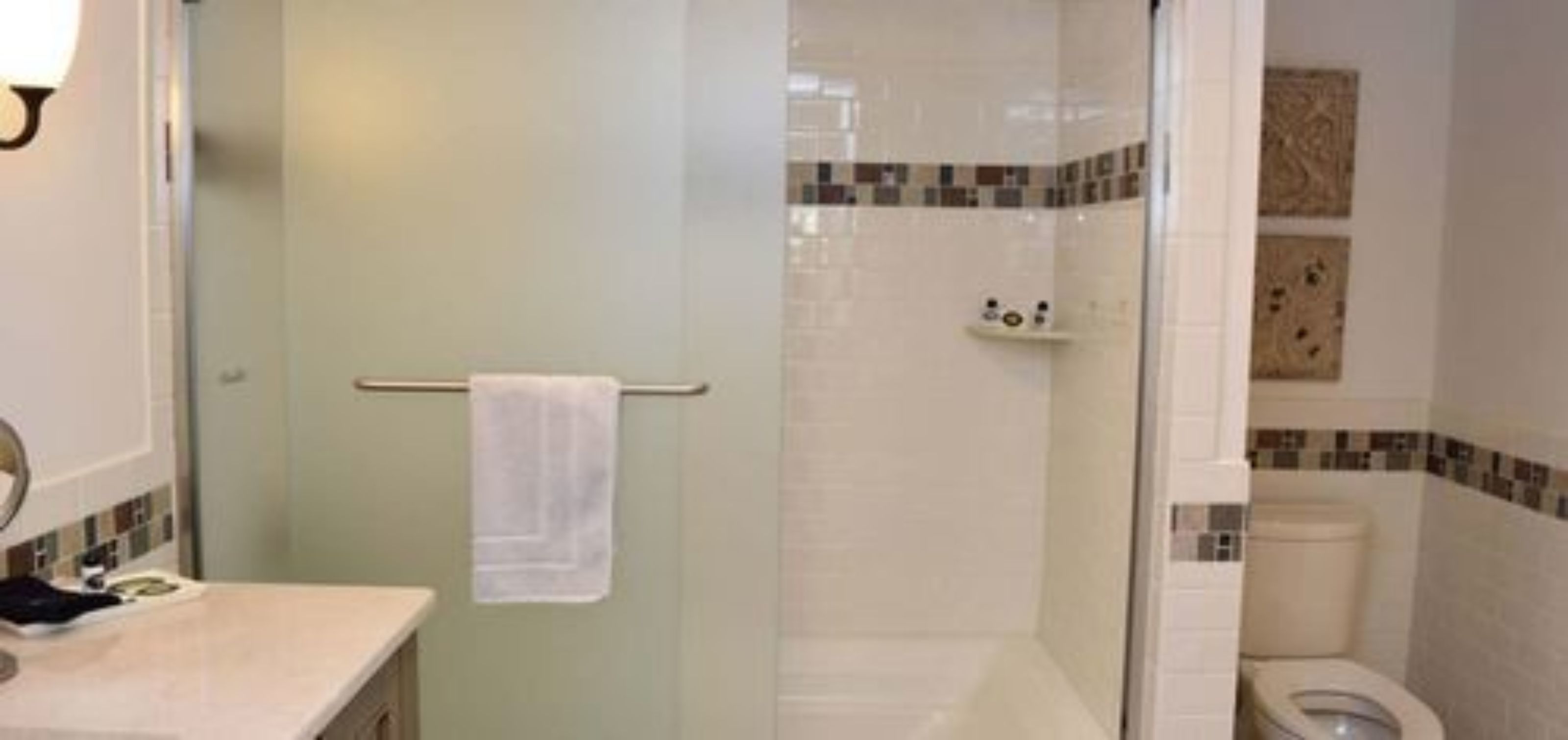 Un baño con cabina de ducha de vidrio, inodoro y lavamanos con una toalla colgada en la puerta.