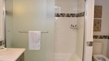 Un baño con cabina de ducha de vidrio, inodoro y lavamanos con una toalla colgada en la puerta.