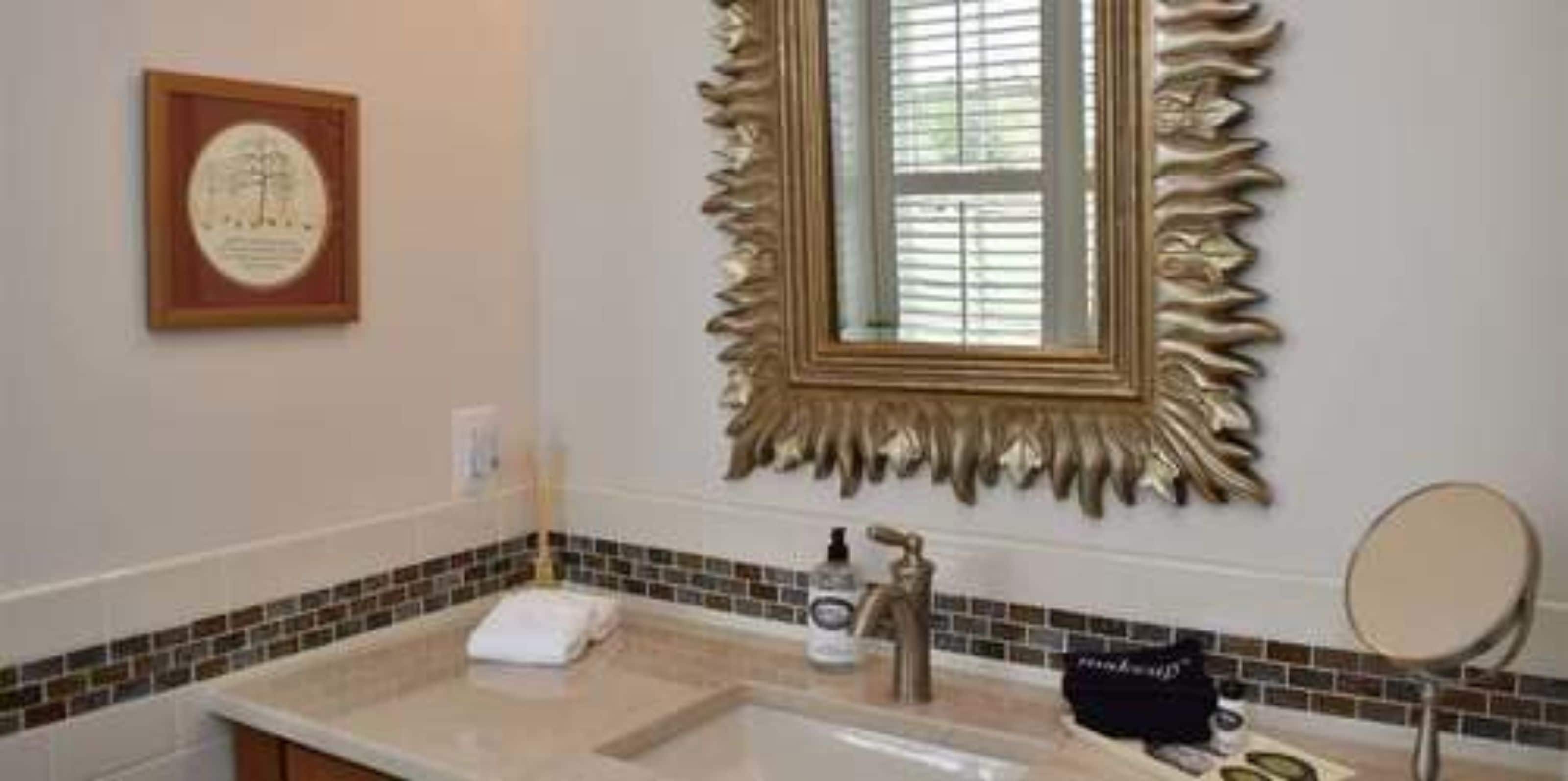 A bathroom with a large mirror, a framed certificate on the wall, and a tiled backsplash.