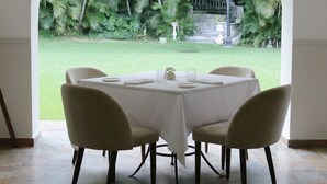 A dining area with a table set for four, an arched doorway leading to a lush garden with palm trees. - Il Buongustaio (San Salvador)