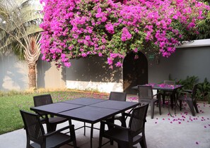 An outdoor patio with a table and chairs, surrounded by lush greenery and vibrant pink flowers. - Il Buongustaio (San Salvador)