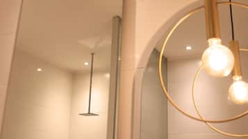 Um banheiro moderno com box de vidro, chuveiro visível e iluminação pendente.