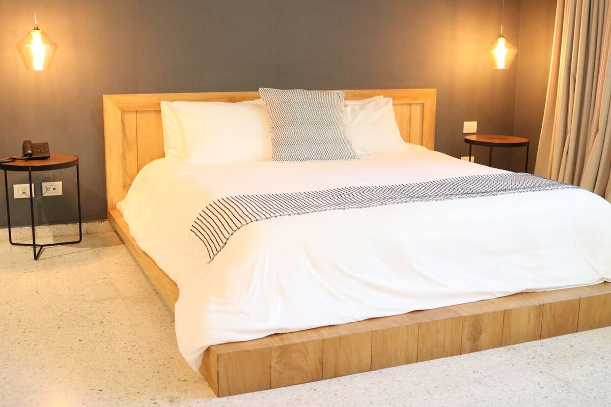 A neatly made bed with a wooden headboard, two bedside tables, and two wall-mounted lights.