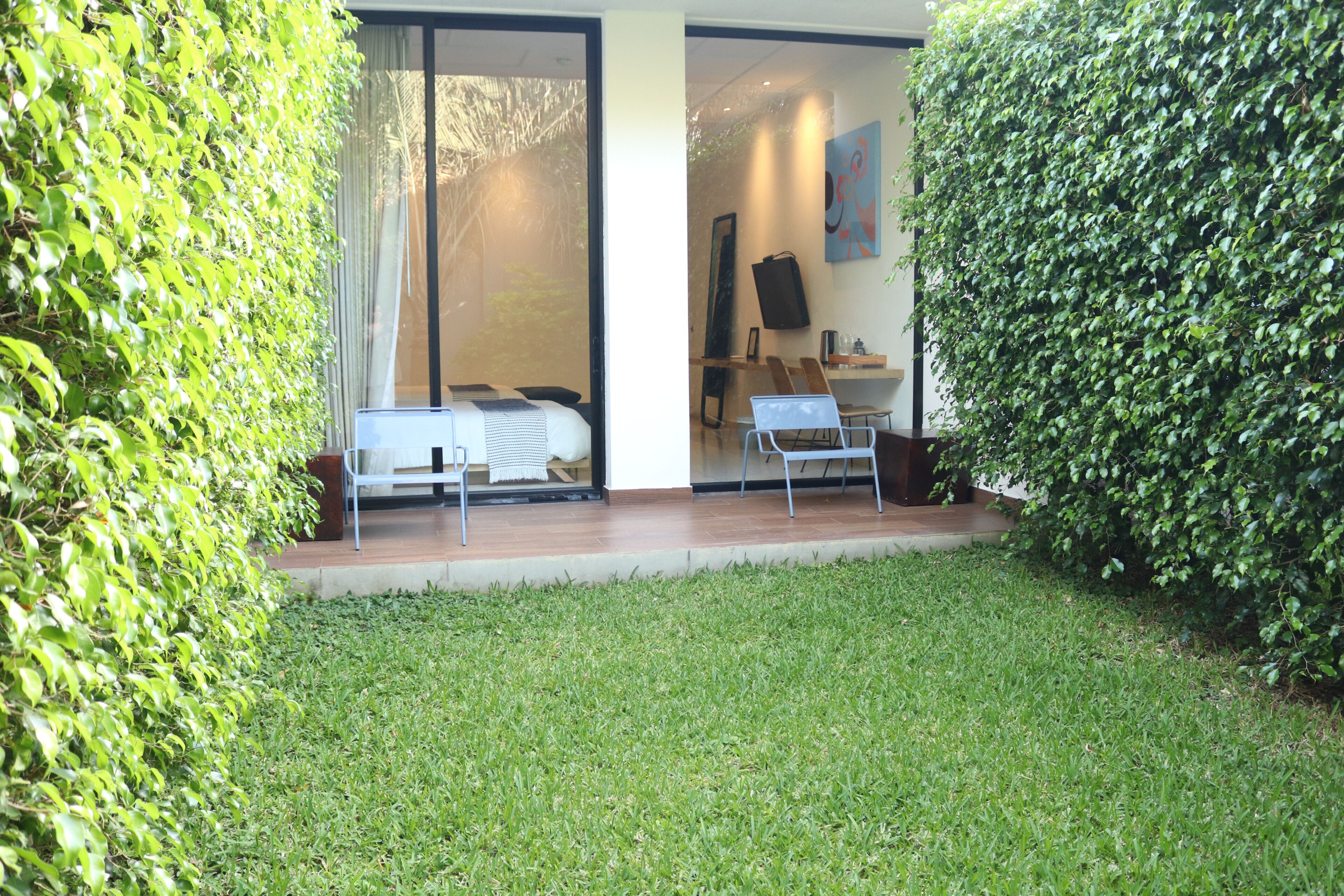 A modern outdoor seating area with a sofa and chairs, a glass door leading to a room, and a well-maintained lawn.