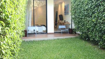 A modern outdoor seating area with a sofa and chairs, a glass door leading to a room, and a well-maintained lawn.