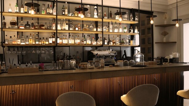 A bar area with shelves of liquor bottles, a coffee machine, and three bar stools. - Il Buongustaio (San Salvador)