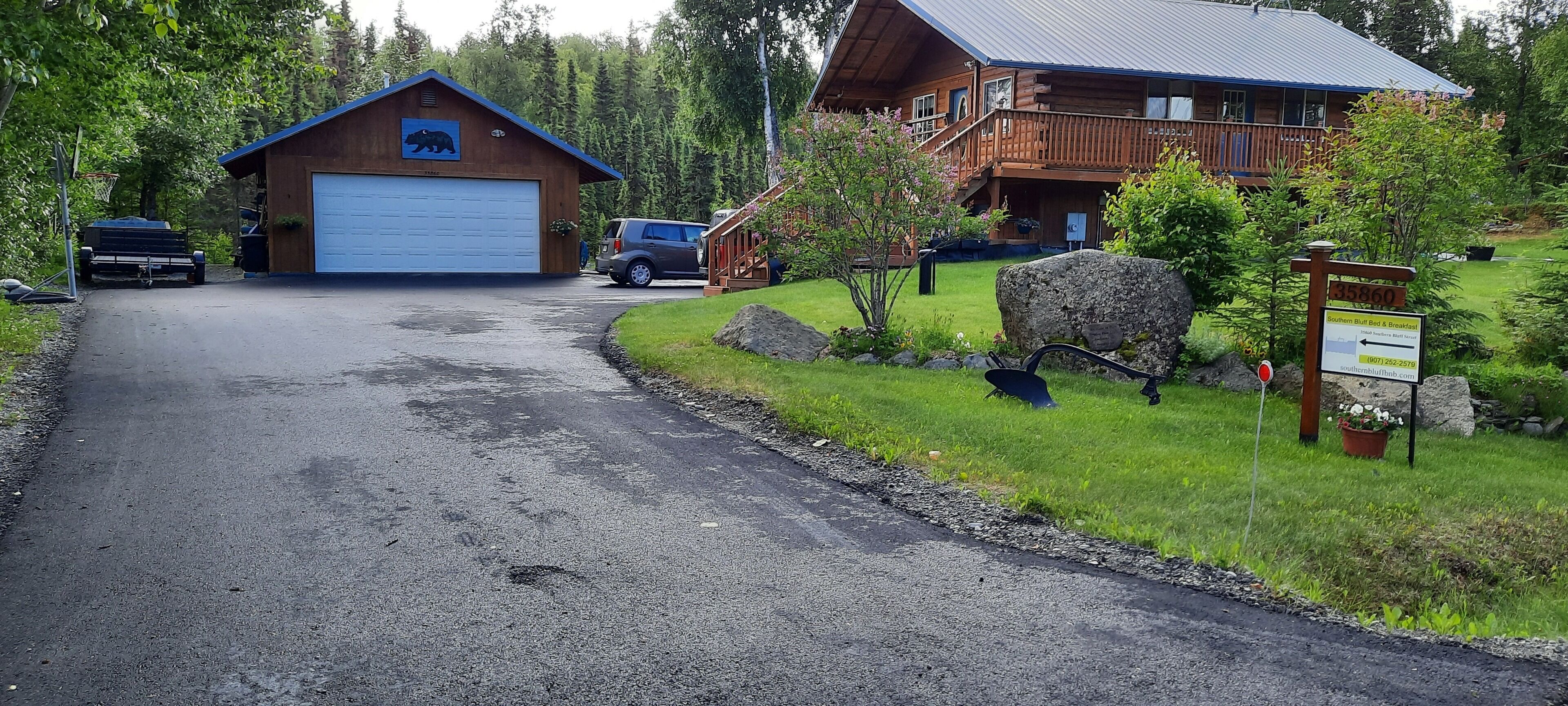 A wooden cabin with a garage and a large rock in the front yard.