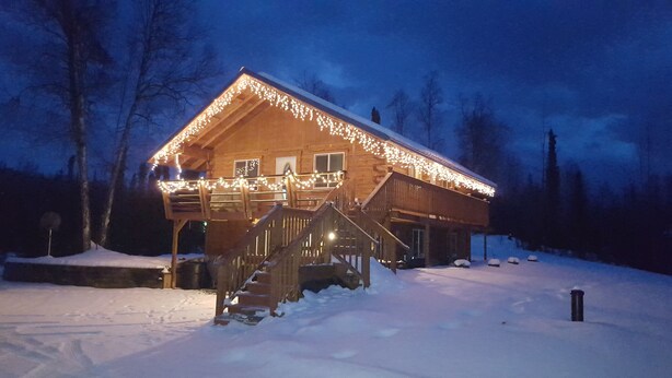 A wooden cabin with a covered porch and stairs leading up to the entrance, surrounded by snow. - Southern Bluff B&B (Soldotna)