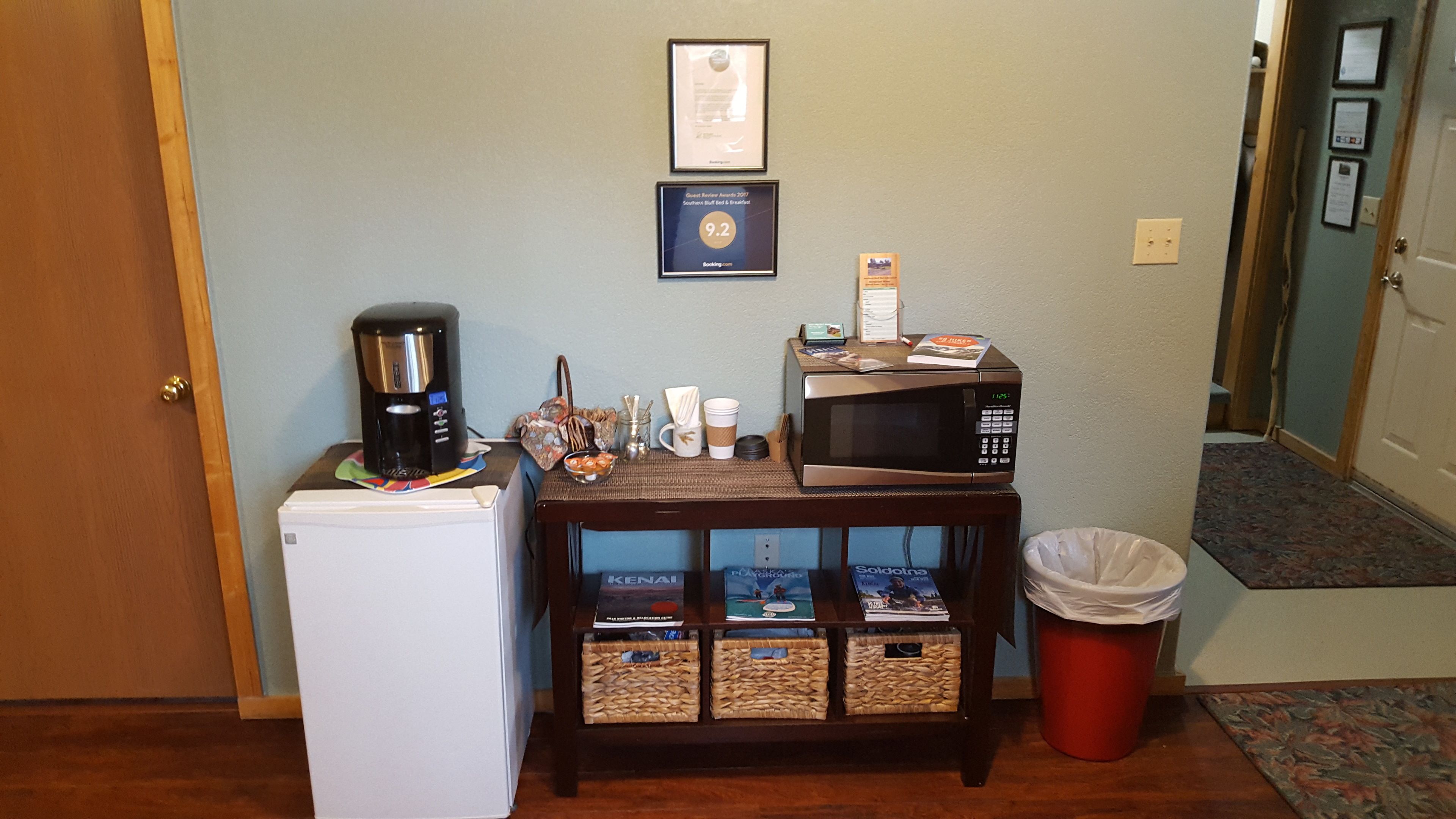 A kitchenette with a coffee maker, microwave, and small refrigerator. There are baskets under the microwave and a trash can next to it.