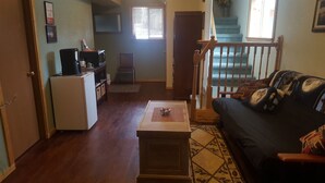 A living room with a dark-colored sofa, a coffee table, a white refrigerator, and a wooden staircase. - Southern Bluff B&B (Soldotna)