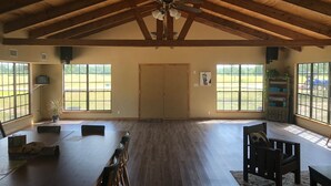 A spacious room with a high ceiling, large windows, a dining area with chairs, and a door.