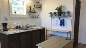 A kitchen with dark wooden cabinets, a granite countertop, a coffee maker, a sink, and a small table. There are potted plants on a shelf above the sink and a towel rack with a blue towel.